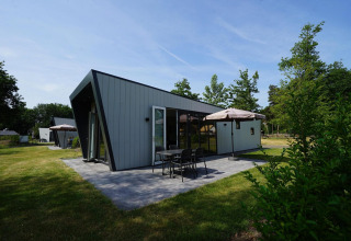 Un lodge moderno de Just Nature en Reestervallei, Países Bajos, con patio, mesa y sombrilla en el jardín.