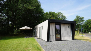 Buitenbeeld van de Just Nature Light lodge met modern design, gazon en zithoek met parasol.