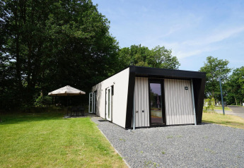 Buitenaanzicht van de Just Nature Light lodge met modern ontwerp, groen gazon en parasolgedeelte.
