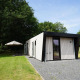 Udendørs foto af Just Nature Light lodge med moderne design, grøn græsplæne og parasolområde.