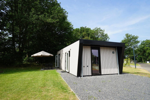 Buitenbeeld van de Just Nature Light lodge met modern design, gazon en zithoek met parasol.