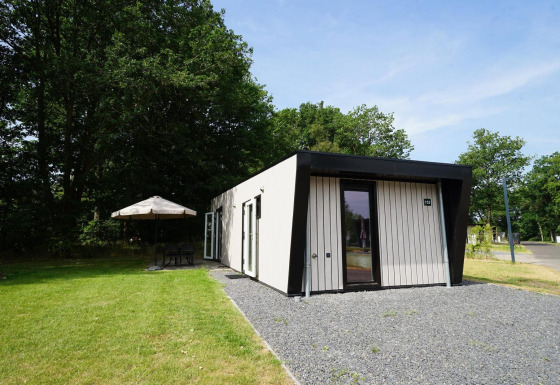 Buitenbeeld van de Just Nature Light lodge met modern design, gazon en zithoek met parasol.