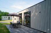 Moderne Lodge Just Nature Light in Reestervallei, Niederlande, mit Terrasse, Tisch, Stühlen und Sonnenschirm.