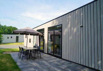 Moderne Lodge Just Nature Light in Reestervallei, Niederlande, mit Terrasse, Tisch, Stühlen und Sonnenschirm.