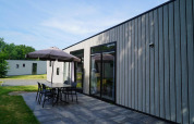 Moderne hytte Just Nature Light ved Reestervallei, Holland, med terrasse, bord, stole og parasol.
