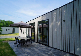 Moderne hytte Just Nature Light ved Reestervallei, Holland, med terrasse, bord, stole og parasol.