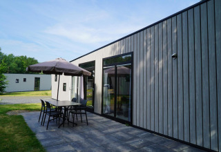 Moderne lodge Just Nature Light bij Reestervallei in Nederland met terras, tafel, stoelen en parasol.