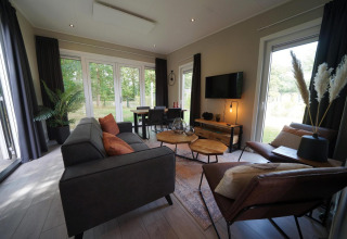 Moderne Just Nature Light lodge in Reestervallei, Nederland, grote ramen en gezellige zithoek met natuurzicht.