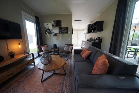 Wohnzimmer der Just Nature Light Lodge in Reestervallei, Niederlande, mit moderner Einrichtung und großen Fenstern.