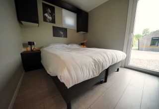 Chambre moderne du lodge Just Nature Light à Reestervallei, Pays-Bas, avec lit double et grande fenêtre.