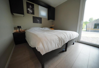 Modern ingerichte slaapkamer in Just Nature Light-lodge bij Reestervallei, Nederland, met tweepersoonsbed en groot raam.