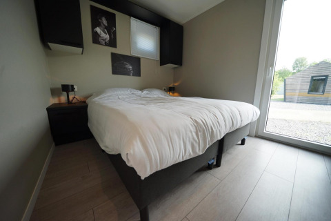 Moderne soveværelse i Just Nature Light-lodge ved Reestervallei, Nederlandene, med dobbeltseng og stor rude.