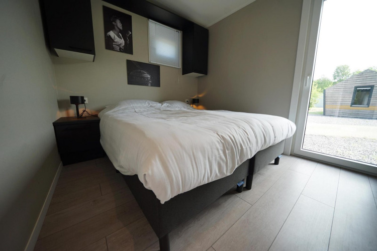 Dormitorio moderno en la cabaña Just Nature Light de Reestervallei, Países Bajos, con cama doble y gran ventanal.