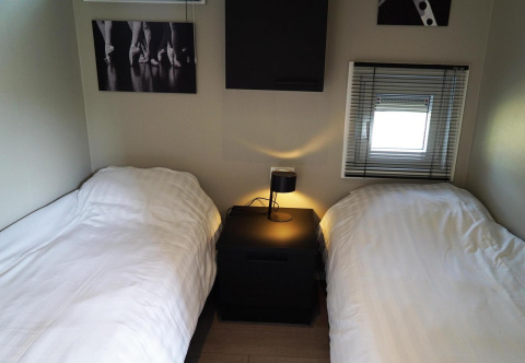 Two single beds with white duvets, a black nightstand and lamp in a lodge at Reestervallei, Netherlands.