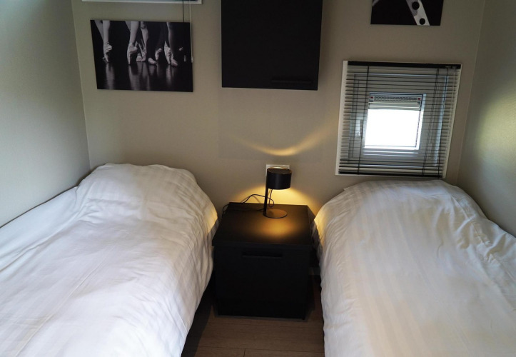 Dos camas individuales con edredones blancos, una mesita y lámpara en una cabaña en Reestervallei, Países Bajos.