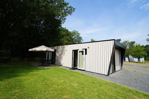 Lyst lodgehus ved Just Nature Light i Reestervallei, Holland, omgivet af grønne træer og græsplæne.