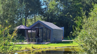 Das Solo Retreat Tiny House am Teich, umgeben von grüner Natur und Bäumen an einem sonnigen Tag.