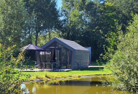 Tiny house Solo Retreat accanto a uno stagno, immersa tra alberi verdi e natura luminosa.