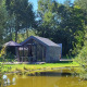 Et billede af Solo Retreat tiny house ved en lille dam, omgivet af grønne træer og natur.