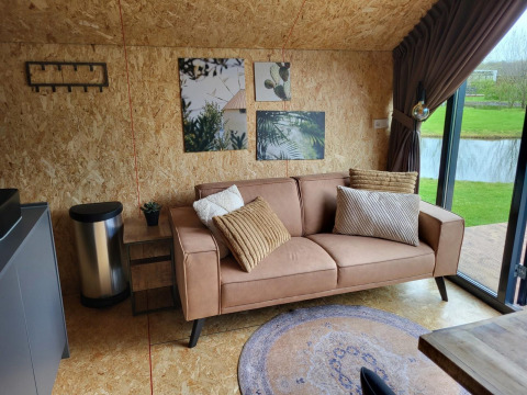Soggiorno moderno in tiny house Solo Retreat a Reestervallei, Paesi Bassi, con divano e vista lago.