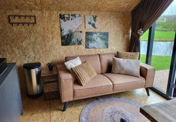 Salon moderne dans un tiny house Solo Retreat à Reestervallei, Pays-Bas, avec canapé et vue sur le lac.