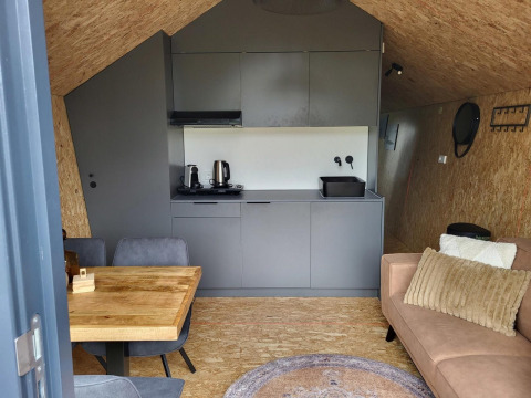 Interno di una tiny house a Reestervallei, Paesi Bassi, con cucina compatta, tavolo e divano.