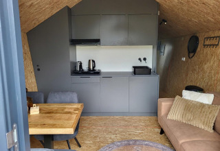 Interior de una tiny house en Reestervallei, Países Bajos, con cocina compacta, mesa y sofá.