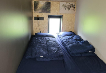 Schlafzimmer im Tiny House Solo Retreat in Reestervallei, Niederlande, mit zwei Betten und dunkelblauer Bettwäsche.