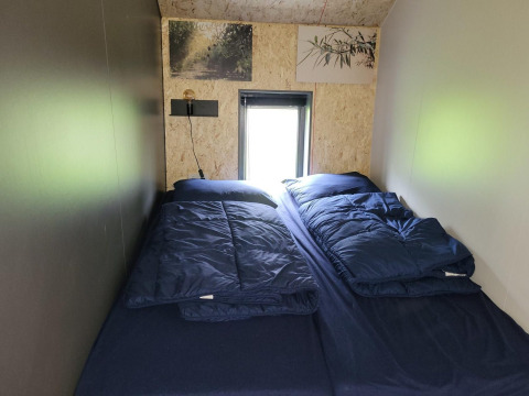 Habitación en la tiny house Solo Retreat en Reestervallei, Países Bajos, con dos camas y ropa azul.