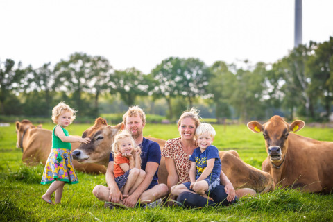 A family with young children sits on grass with brown cows at FarmCamps BoeBaDoe holiday park in Limburg.