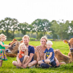 Una familia con niños pequeños se sienta en el pasto junto a vacas marrones en FarmCamps BoeBaDoe, Limburg.