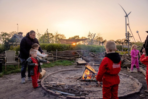 Kinderen en volwassenen roosteren marshmallows bij een kampvuur bij zonsondergang in FarmCamps BoeBaDoe, Limburg.