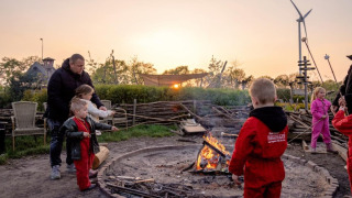 Niños y adultos asan malvaviscos al atardecer junto a una fogata en FarmCamps BoeBaDoe, Limburg, Países Bajos.
