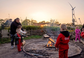 Kinderen en volwassenen roosteren marshmallows bij een kampvuur bij zonsondergang in FarmCamps BoeBaDoe, Limburg.