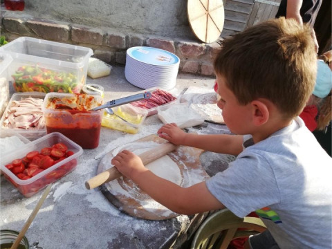Niño extiende masa de pizza rodeado de ingredientes frescos en FarmCamps BoeBaDoe en Limburg, Países Bajos.