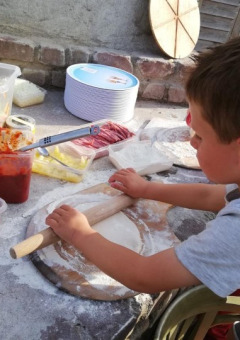 Niño extiende masa de pizza rodeado de ingredientes frescos en FarmCamps BoeBaDoe en Limburg, Países Bajos.