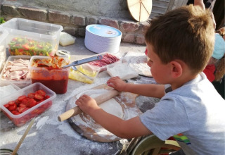 Junge rollt Pizzateig aus, umgeben von frischen Zutaten, bei FarmCamps BoeBaDoe in Limburg, Niederlande.