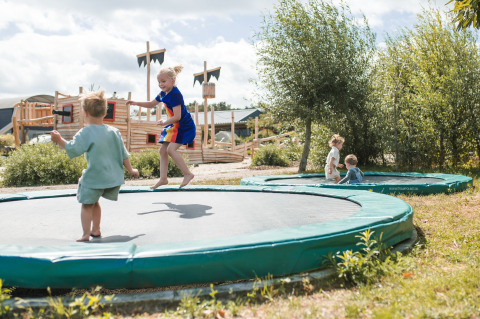 Kids play on sunken trampolines at FarmCamps BoeBaDoe holiday park in Limburg, Netherlands, on a sunny day.