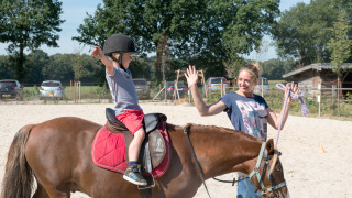 Un niño aprende a montar a caballo con la ayuda de una instructora en FarmCamps BoeBaDoe, Limburg.