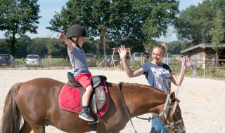 Un niño aprende a montar a caballo con la ayuda de una instructora en FarmCamps BoeBaDoe, Limburg.
