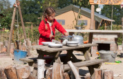 Mädchen im roten Anzug spielt draußen an einem Holztisch im FarmCamps BoeBaDoe in Limburg, Niederlande.