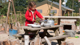 Meisje in rode jas speelt met servies aan een buitentafel bij FarmCamps BoeBaDoe in Limburg, Nederland.