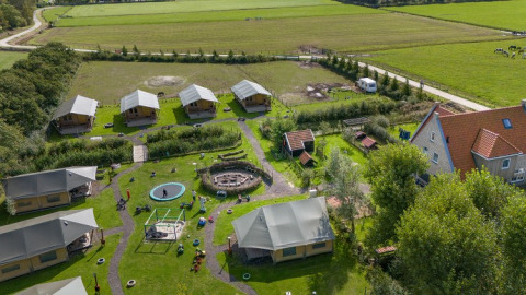 Vista aérea de FarmCamps De Bonte Fries en Frisia, Países Bajos, con tiendas, patio de juegos y campos verdes.