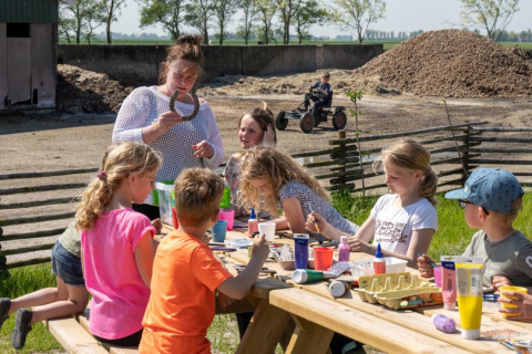 Niños haciendo manualidades al aire libre con un adulto en FarmCamps De Bonte Fries, parque vacacional en Frisia, Países Bajos.