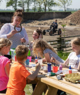 Niños haciendo manualidades al aire libre con un adulto en FarmCamps De Bonte Fries, parque vacacional en Frisia, Países Bajos.