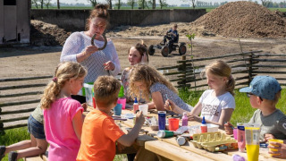 Niños haciendo manualidades al aire libre con un adulto en FarmCamps De Bonte Fries, parque vacacional en Frisia, Países Bajos.