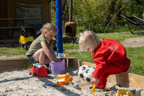 Twee kinderen spelen met zand en speelgoed in de zandbak op FarmCamps De Bonte Fries in Friesland, Nederland.