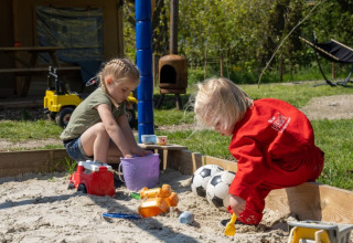 Two children play with sand and toys in a sandbox at FarmCamps De Bonte Fries in Friesland, Netherlands.