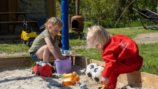 Dos niños juegan con arena y juguetes en un arenero en FarmCamps De Bonte Fries en Frisia, Países Bajos.