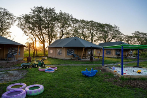 Speelplein met zandbak, speelgoed en safaritenten bij zonsondergang op FarmCamps De Bonte Fries in Friesland.